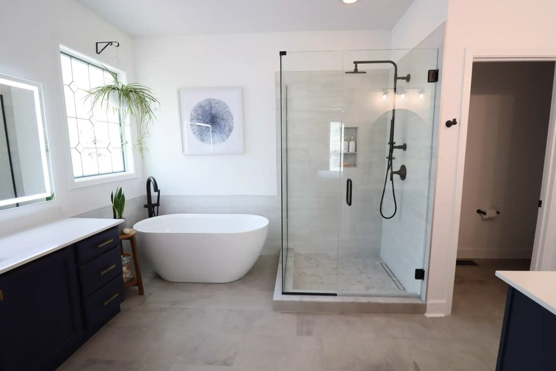 Frameless hinged shower door with matte black hardware, paired with a freestanding tub in a bright primary bathroom.