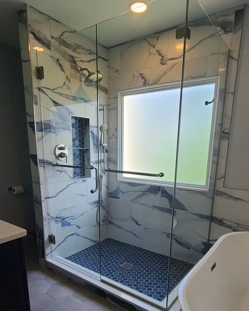 Frameless corner shower with matte black clips, blue hexagon mosaic floor, and dramatic blue-veined marble walls.