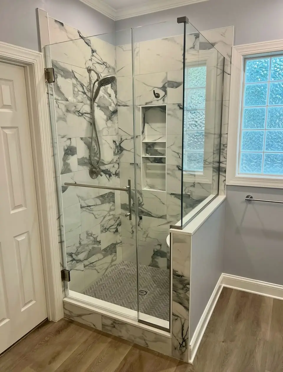 Frameless shower with hinged door and knee-wall return panel, brushed nickel hardware, and dramatic veined marble.