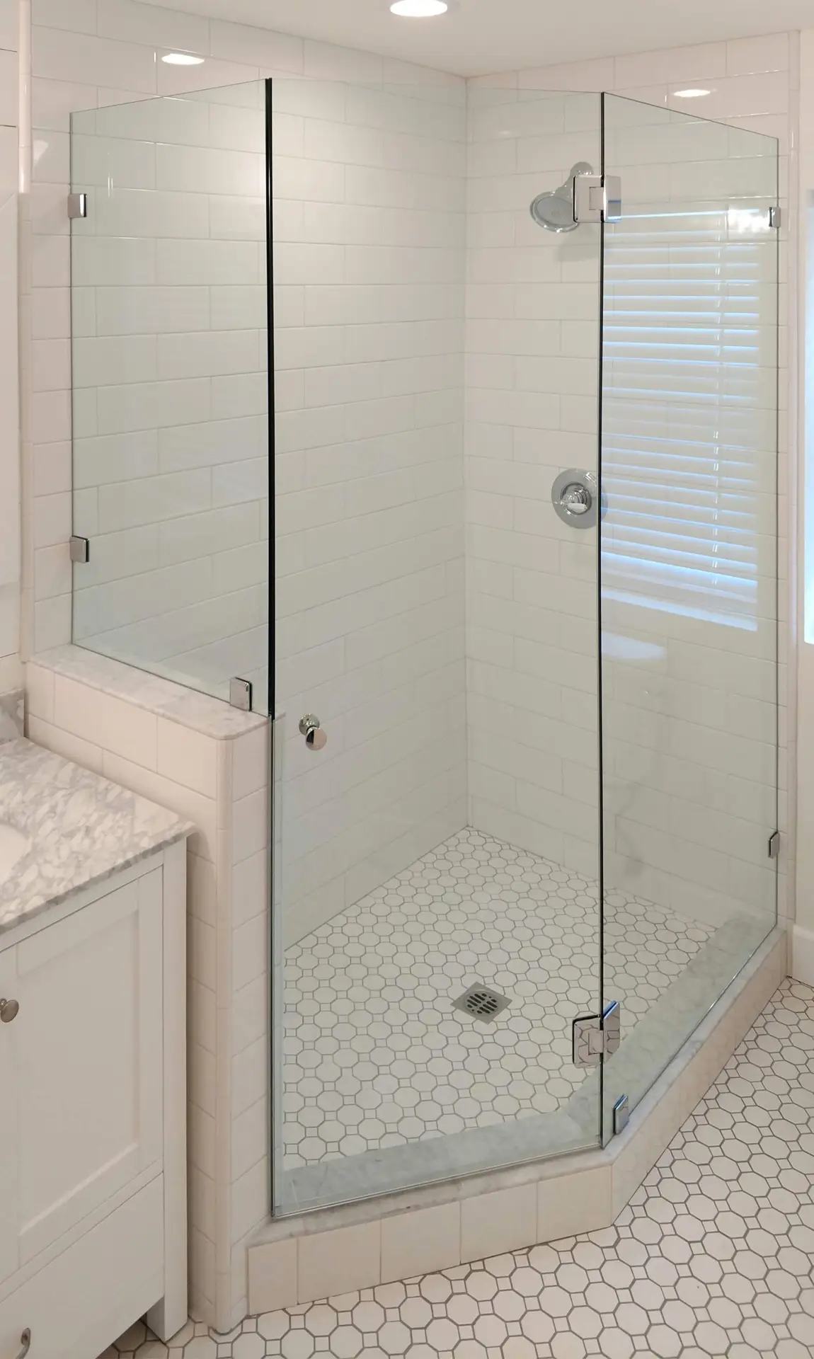 Frameless neo-angle shower in a small bathroom with white subway tile, polished chrome hardware, and an octagon-and-dot mosaic floor.