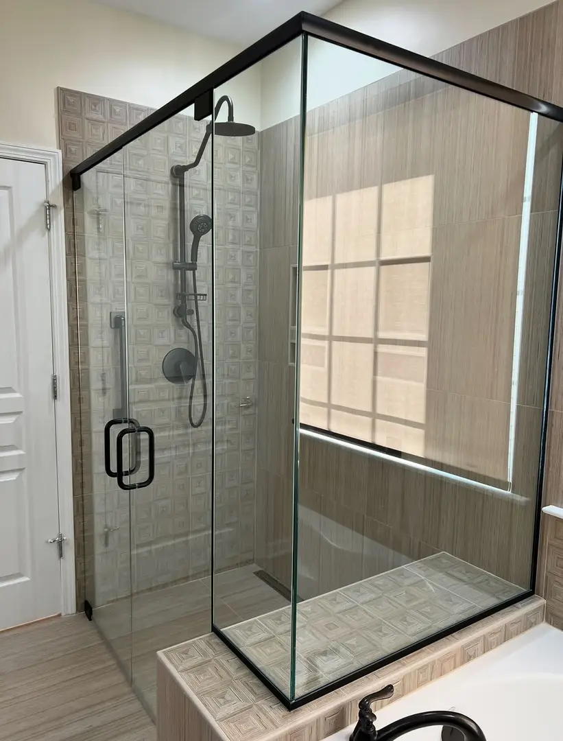 Semi-frameless 90-degree shower enclosure with matte black header rail and matching hardware over a soaking tub.