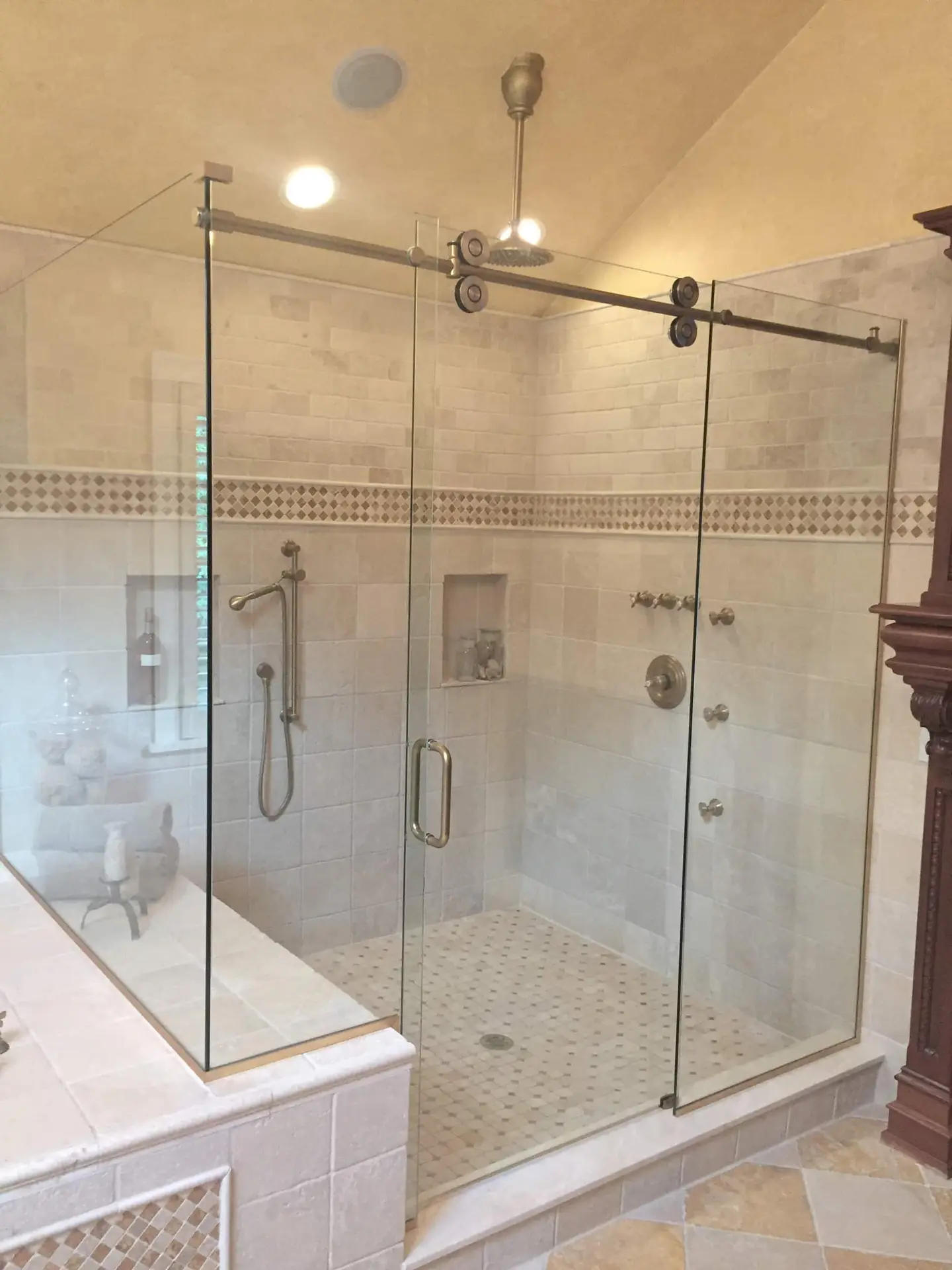 Frameless Euroglide-style sliding shower door over a corner enclosure with brushed nickel barn-door hardware and travertine walls.