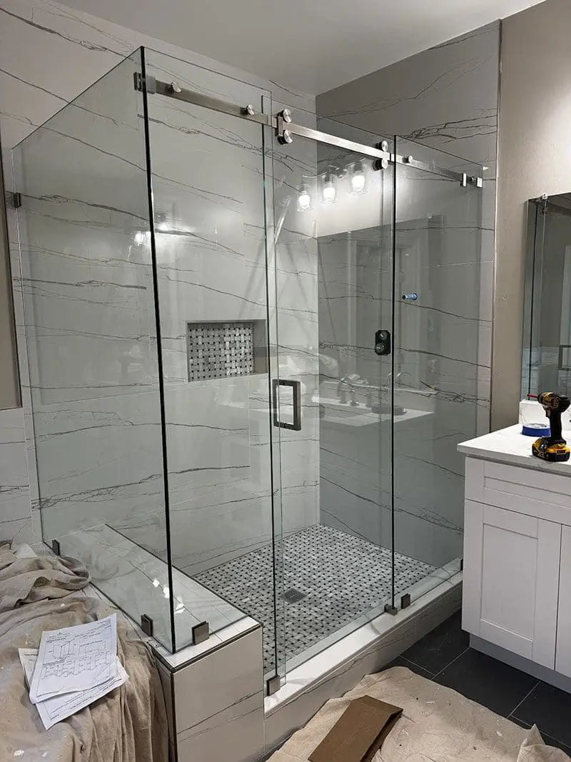 Frameless corner shower enclosure with sliding center door, brushed nickel hardware, and white quartzite walls.