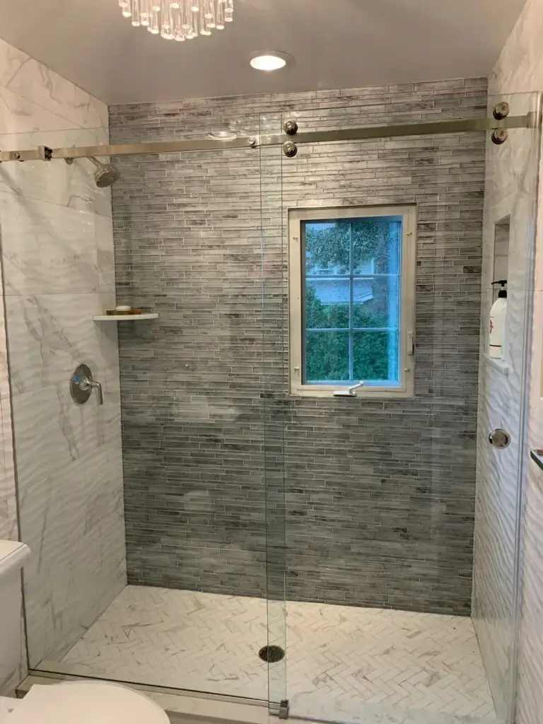 Frameless Slimglide single sliding shower door in a stall configuration with brushed nickel hardware and herringbone marble floor.